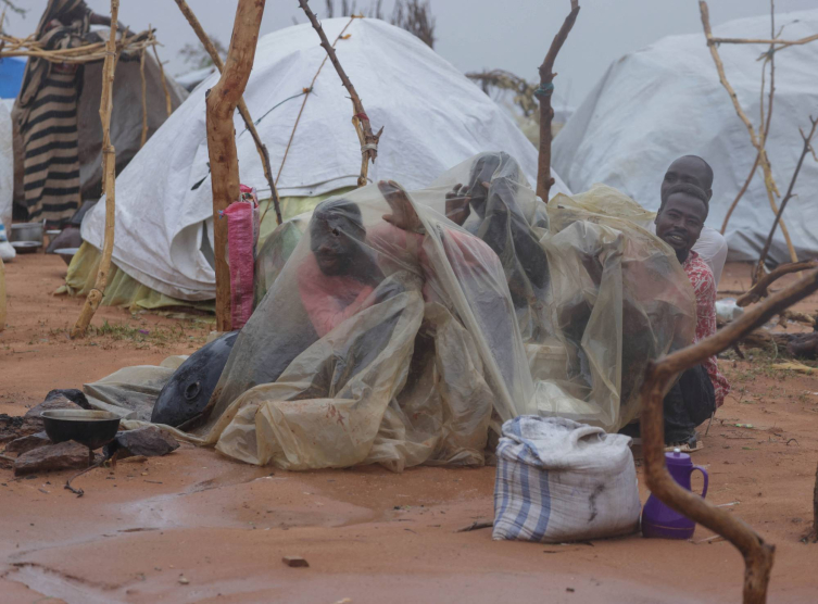 Darfur'dan kaçarak komşu ülke Çad'daki bir mülteci kampına sığınan Sudanlılar sağanak yağmurdan naylon örtüyle korunmaya çalışıyor. (Reuters)